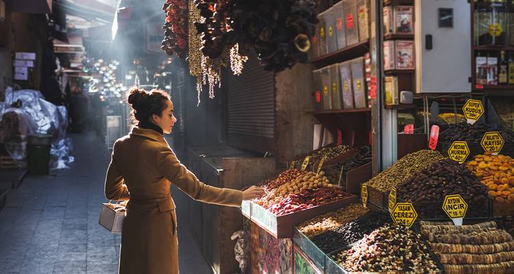 Ochtendlicht stroomt door Istanbuls kruidenbazaar terwijl een winkelier kleurrijke stapels gedroogd fruit en kruiden inspecteert.