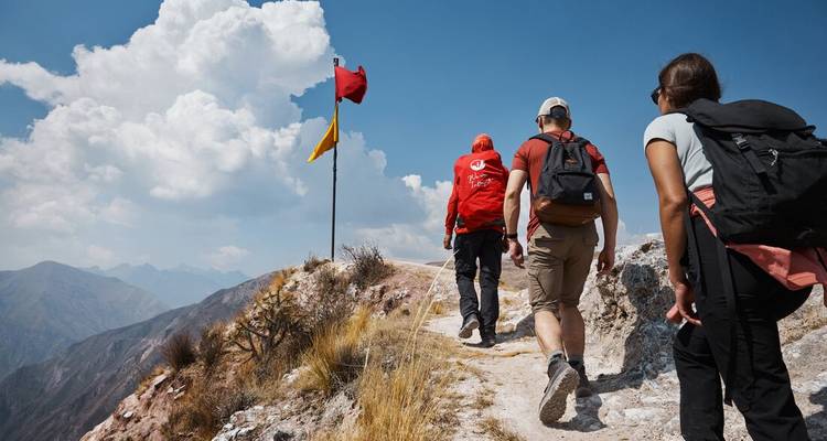 Wanderer auf einem Pfad mit einer roten Flagge auf einem Hügel mit Bergen in der Ferne.