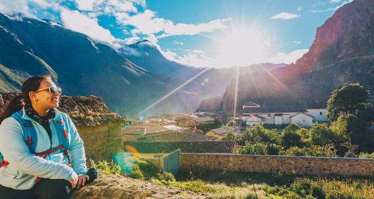 Person sitting on a rock enjoying a scenic mountain view with the sun shining.