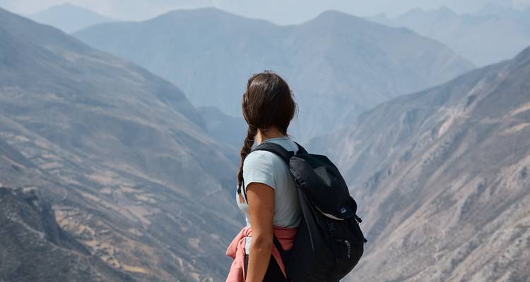 Femme avec un sac à dos regardant un vaste paysage de montagnes.