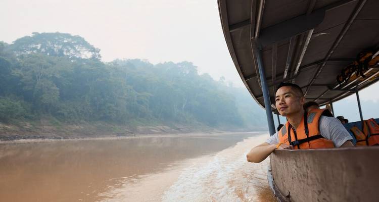 Une personne dans un bateau portant un gilet de sauvetage, naviguant sur une rivière avec une forêt luxuriante sur les rives.