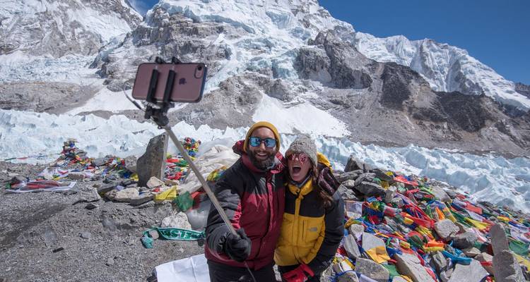 Enthousiast stel maakt een selfie met smartphone op een stok op Everest Base Camp omringd door gebedsvlaggen en ijs.