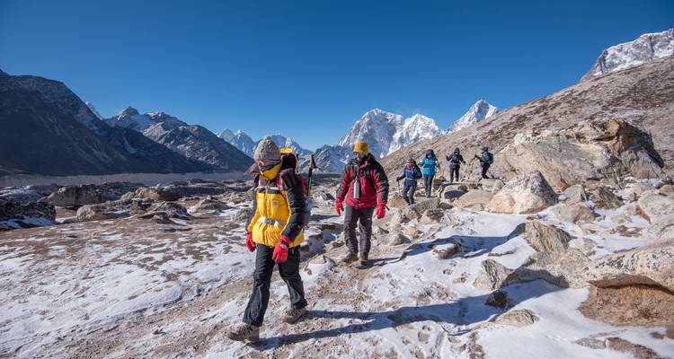 Trekkers steken een licht met sneeuw bedekt rotsachtig landschap over onder een frisse, heldere Himalaya-lucht.
