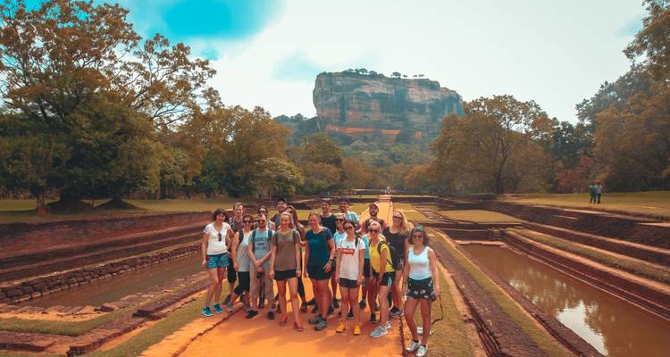 A group of people posing in front of an ancient fortress or rock.