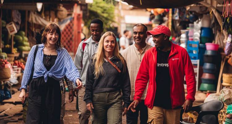 Group of travellers walk through a vibrant local market lined with produce and colourful goods.
