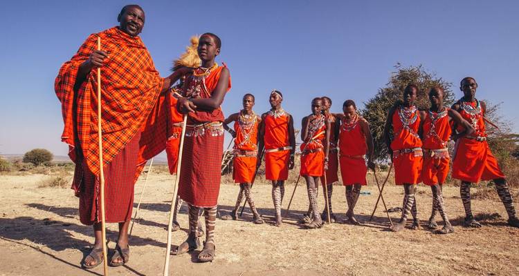 Line of Maasai men dressed in bright red shukas performing traditional dance on open savannah.