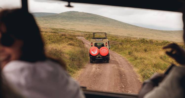 Tourists in a vehicle on a dirt road, following another vehicle in a rugged landscape.