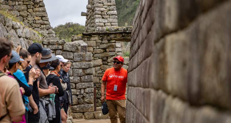 Un guía con una camisa roja brillante habla con los viajeros entre las paredes de piedra y las entradas de Machu Picchu.