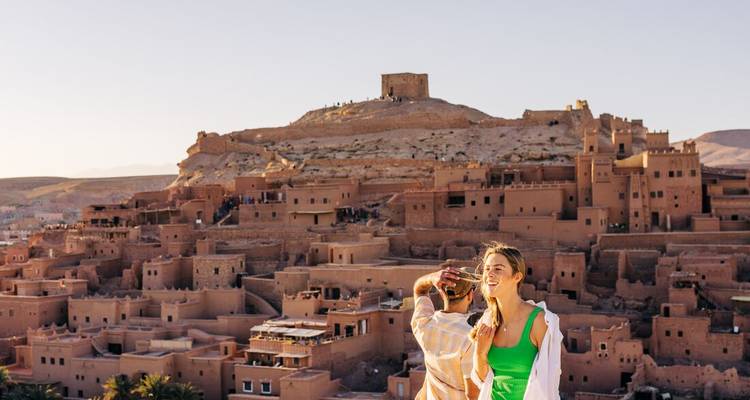 Pareja disfrutando de la vista del atardecer sobre la antigua kasbah de tierra y la fortaleza en la colina del desierto