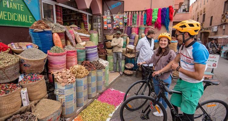 Ciclistas charlando junto a sacos coloridos de especias en un animado puesto de mercado
