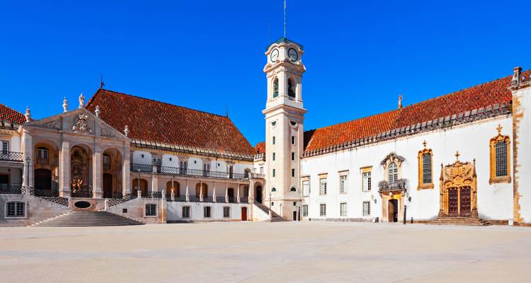 Cour historique de l'Université de Coimbra avec tour de l'horloge et chapelle ornée sous un ciel dégagé.