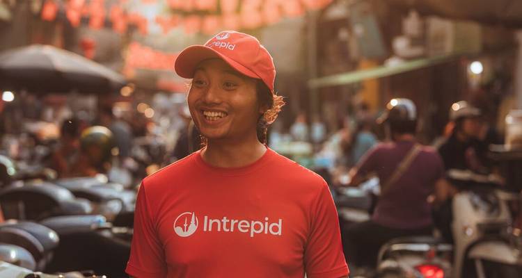 Guide Intrepid souriant vêtu d'une chemise rouge et d'une casquette dans un marché de rue animé de Hanoï