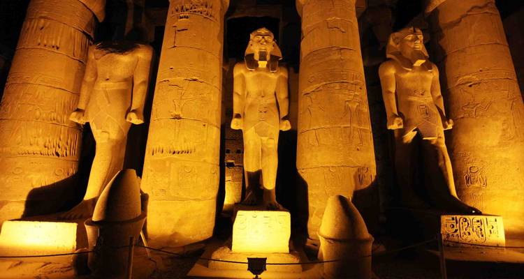 Estatuas y columnas iluminadas de un templo egipcio por la noche