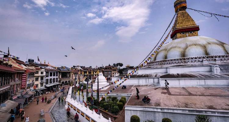 La enorme Estupa Boudhanath blanca de Katmandú se eleva sobre una plaza bulliciosa adornada con banderas de oración ondeantes y pájaros que vuelan en círculos.