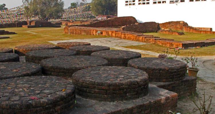 Las ruinas de ladrillos circulares yacen en el sitio budista sagrado de Lumbini junto a un muro de templo blanco moderno.