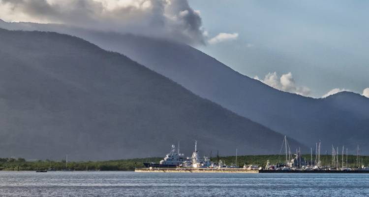 Un elegante yate blanco anclado en una bahía tranquila con montañas boscosas y brumosas elevándose al fondo.