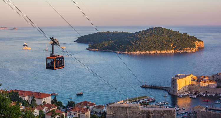 Téléphérique glissant au-dessus de Dubrovnik avec la lumière du soir sur l'Adriatique bleue et l'île voisine.