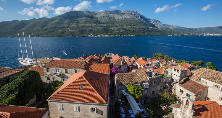 Vue depuis le toit surplombant les maisons en pierre de la vieille ville de Korčula avec une montagne imposante de l'autre côté du chenal bleu profond.