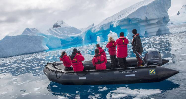 Petit bateau pneumatique avec photographes passant devant des formations d'iceberg en arche bleue