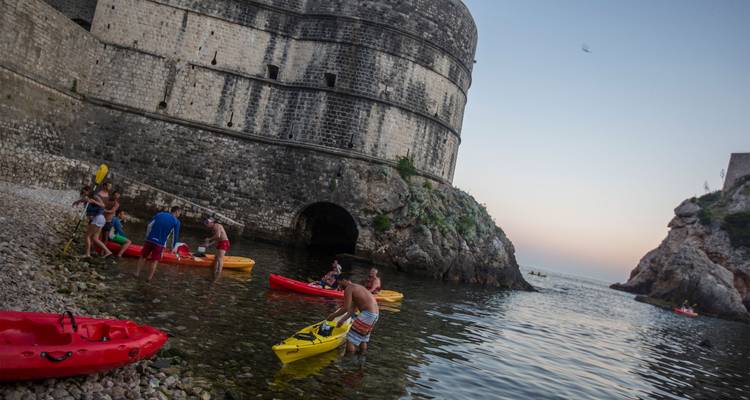 Grupos lanzando kayaks coloridos junto a los muros de fortaleza de piedra de Dubrovnik al atardecer.