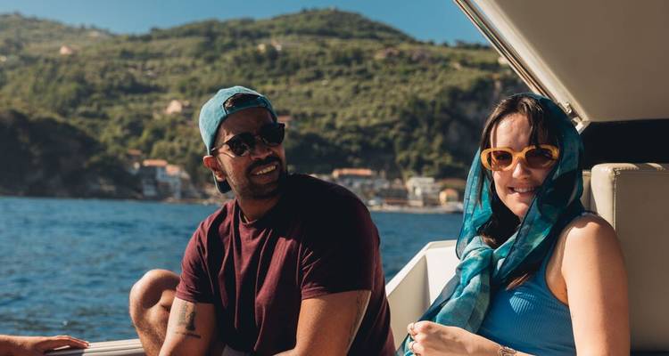 Two friends relaxing on a boat with coastal hills and blue water in the background