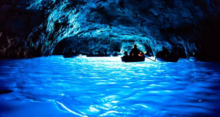 Rowboats inside the glowing blue waters of a sea cave illuminated by reflected light
