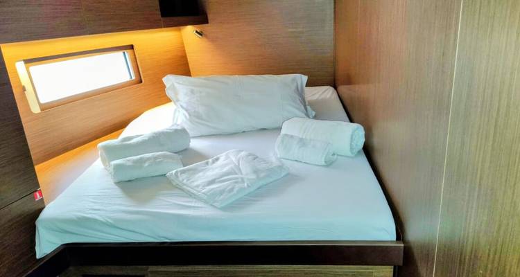 Compact yacht cabin with neatly made double bed, towels, and warm wood paneling.