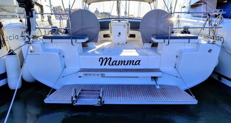 Stern view of a white sailing yacht named “Mamma” docked at a marina.