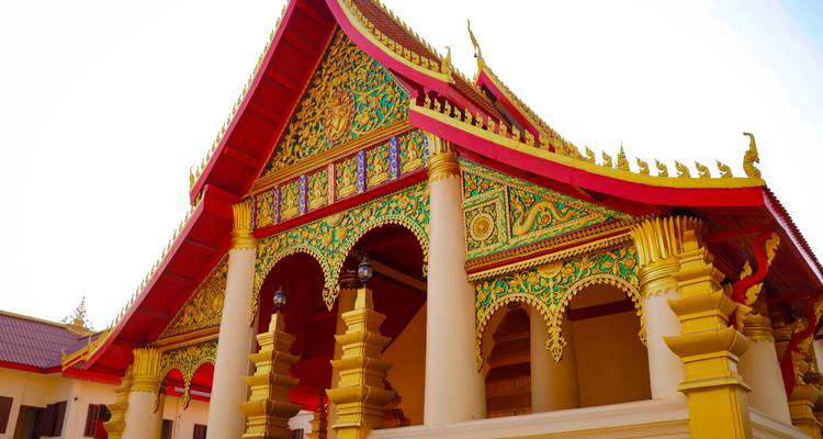 Toit et arches de temple lao aux décorations éclatantes se détachant sur un ciel blanc