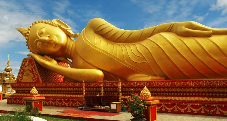 Statue massive de Bouddha couché doré scintillant sous un ciel bleu parsemé de nuages