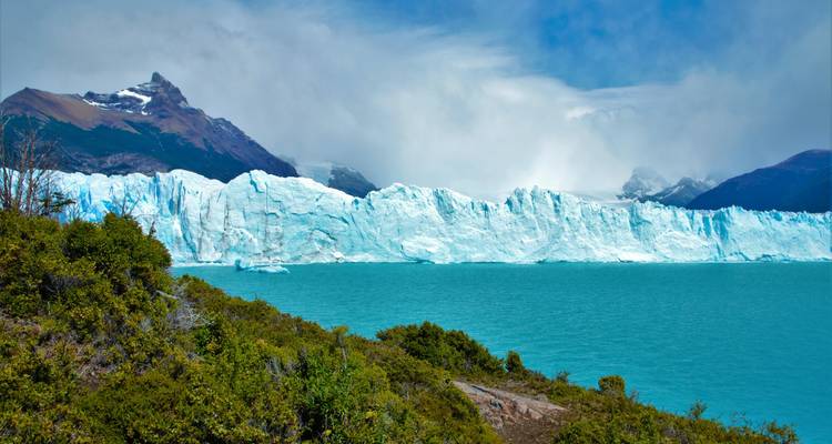Massive glacier meeting a blue lake under dramatic clouds