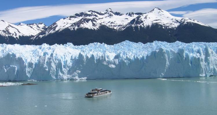Large glacier with a boat in a lake under snowy mountains