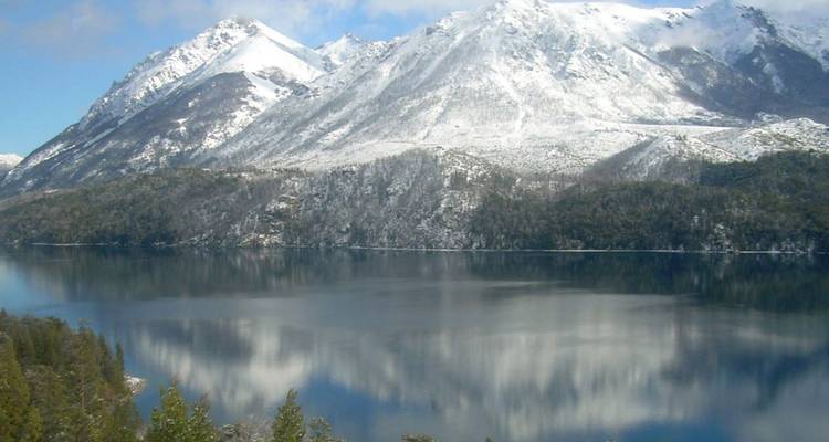 A calm alpine lake reflecting snow-covered peaks and forested slopes near Bariloche.