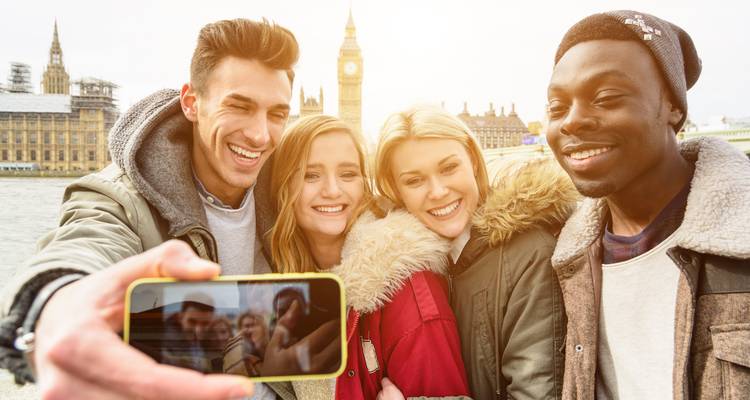 A group of friends takes a joyful selfie with Big Ben and the Houses of Parliament blurred in the background.
