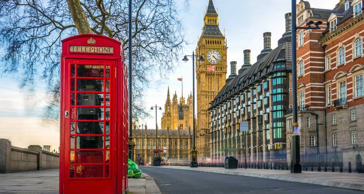 A classic red telephone box frames the view of Big Ben and Westminster’s historic buildings at dawn.