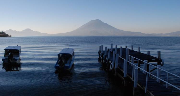 Lago tranquilo con botes y un volcán al fondo.