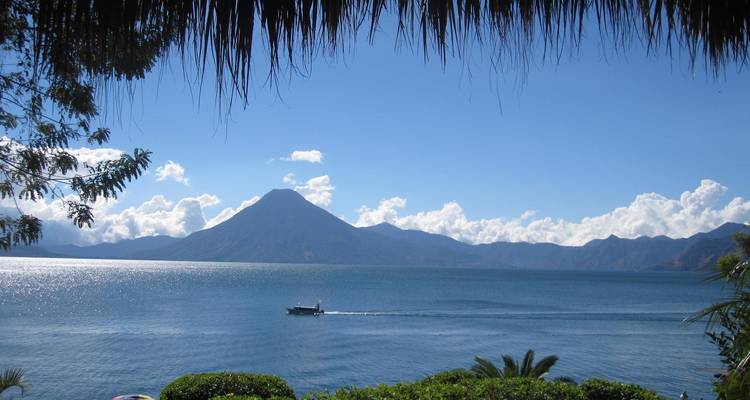 Vista panorámica de un lago con un barco y volcanes en la distancia.