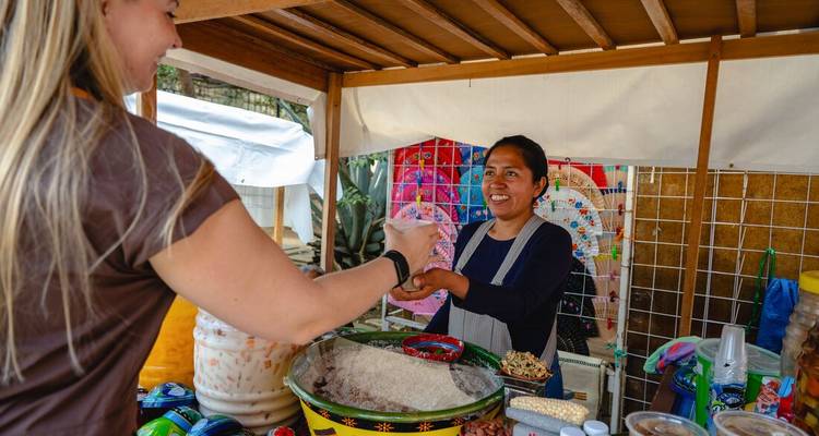 Tourist buys a traditional drink from a smiling vendor at a Mexican market stall.
