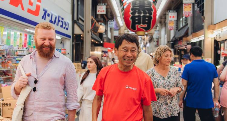 Le guide touristique guide les voyageurs à travers le marché animé de Kuromon à Osaka, bordé de boutiques et d'enseignes.