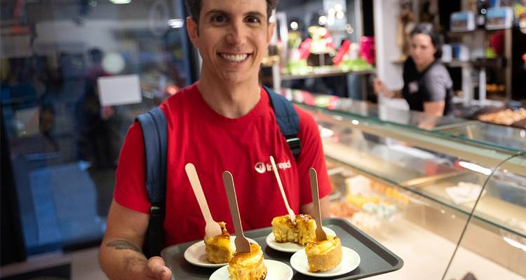 Individuo sosteniendo postres en una bandeja en una tienda.