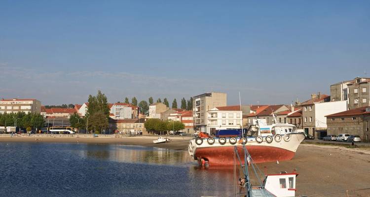 Pequeño puerto con un barco varado y pueblo costero.
