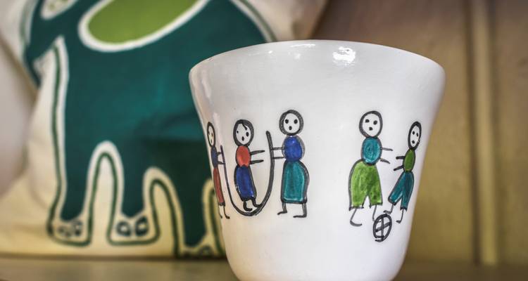 Hand-painted ceramic cup with simple childlike figures displayed on a shelf.