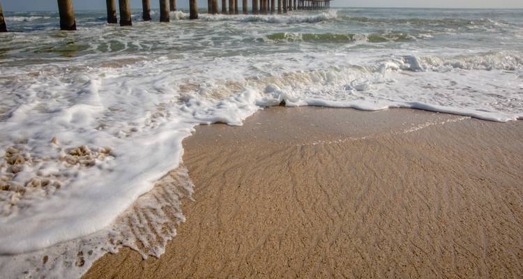 Les vagues écumantes se déversent sur une plage de sable fin à côté d'une longue jetée s'étendant dans l'océan.