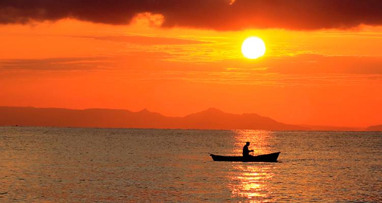 Un pescador solitario rema en un bote pequeño atravesando un lago tranquilo al atardecer ardiente