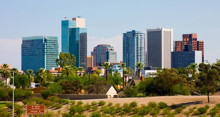 Les gratte-ciel modernes du centre-ville de Phoenix s'élevant au-dessus des palmiers et de la végétation désertique par une journée dégagée.