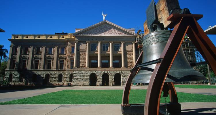 Bâtiment historique du Capitole de l'État de l'Arizona avec une réplique de la Cloche de la Liberté sur un ciel bleu profond.