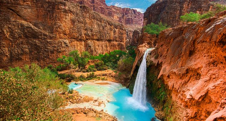 Levendige turquoise Havasu Falls die naar beneden stroomt in een blauw zwembadje in een steile rode rotscanyon.