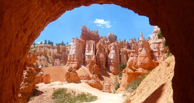 Uitzicht op Bryce Canyon hoodoos door een grot-achtige rode rotsformatie tegen een diepblauwe hemel.
