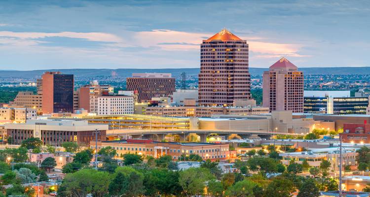 Paisaje urbano al atardecer de Albuquerque con edificios iluminados contra un cielo nocturno en tonos pastel