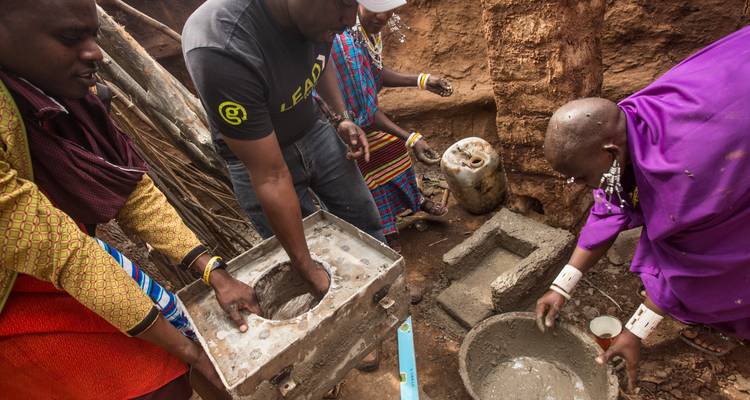 Les visiteurs et les villageois Maasai construisent ensemble un foyer en béton à l'intérieur d'une fosse en terre.